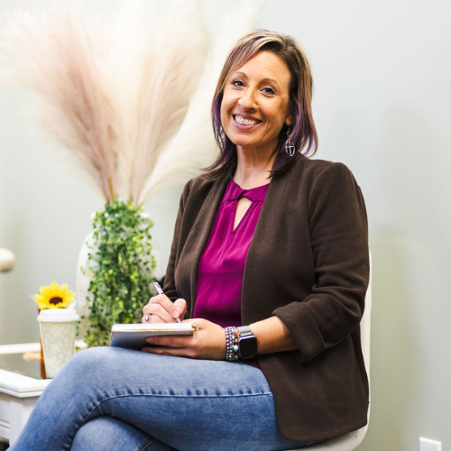 Woman sitting and writing in a notebook with a plant and decorative items in the background